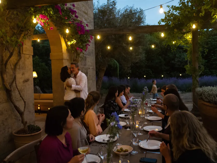 Guests at a dinner under a pergola with string lights; a couple embracing under a stone arch with bougainvillea